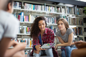 High school students studying together in a library with a digital tablet