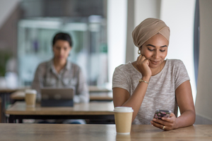 Young adult Muslim female using a smartphone in a cafe