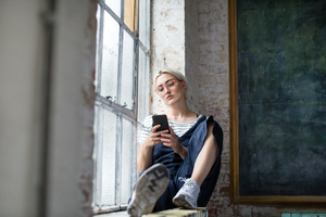 Millennial using smartphone by window in a loft apartment