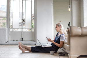 Millennial using smartphone and laptop in a loft apartment