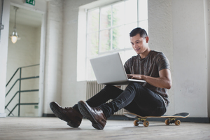 Young adult male working on laptop with skateboard