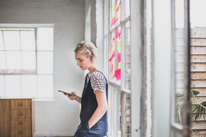 Young adult female using smartphone in a creative office with adhesive notes