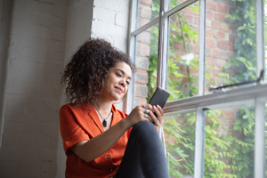 Millennial female using smartphone by window in loft apartment
