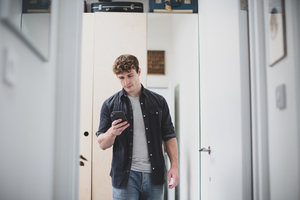 Young adult male using smartphone while walking through home