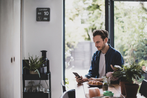 Adult male checking smartphone in kitchen with mug of coffee