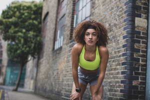 Young adult female taking a break on a run in urban city