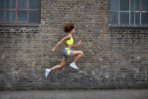 Young adult female leaping in the air with brick wall backdrop