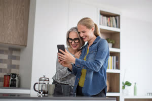 Mature adult woman with grown up daughter looking at smartphone in kitchen