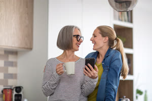 Mature adult woman with grown up daughter looking at smartphone in kitchen