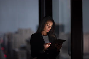 Businesswoman working late using digital tablet with city skyline in background