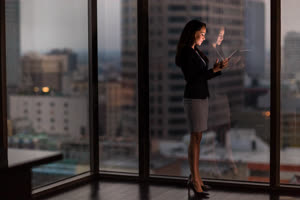 Businesswoman working late using digital tablet with city skyline in background