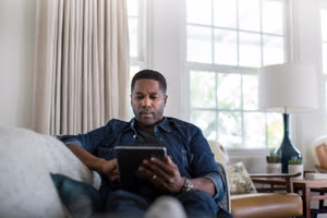 African American adult male using digital tablet at home on sofa