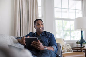 African American adult male using digital tablet at home on sofa