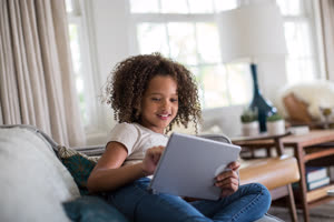 African American girl using digital tablet at home on sofa