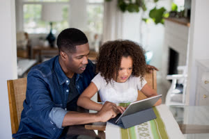 African American father helping daughter with homework using digital tablet