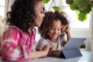 African American mother helping daughter with homework using digital tablet