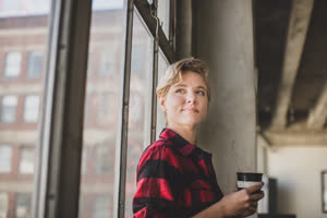 Young female looking out of window in loft apartment thinking