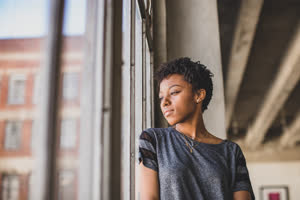 Young african american female looking out of window in loft apartment thinking