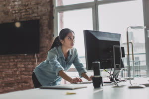 Young adult female standing and working on a desktop computer